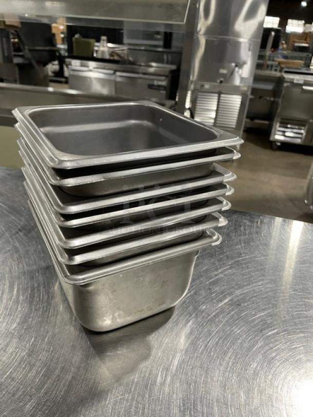 Stack of seven commercial stainless steel hotel pans on a metal surface. Used condition, ideal for steam tables.