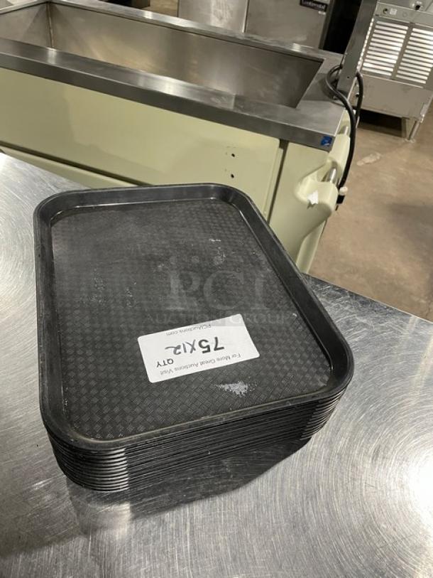 Stack of Cambro black fast food trays on stainless steel surface, label indicating 12X quantity, showing light wear.