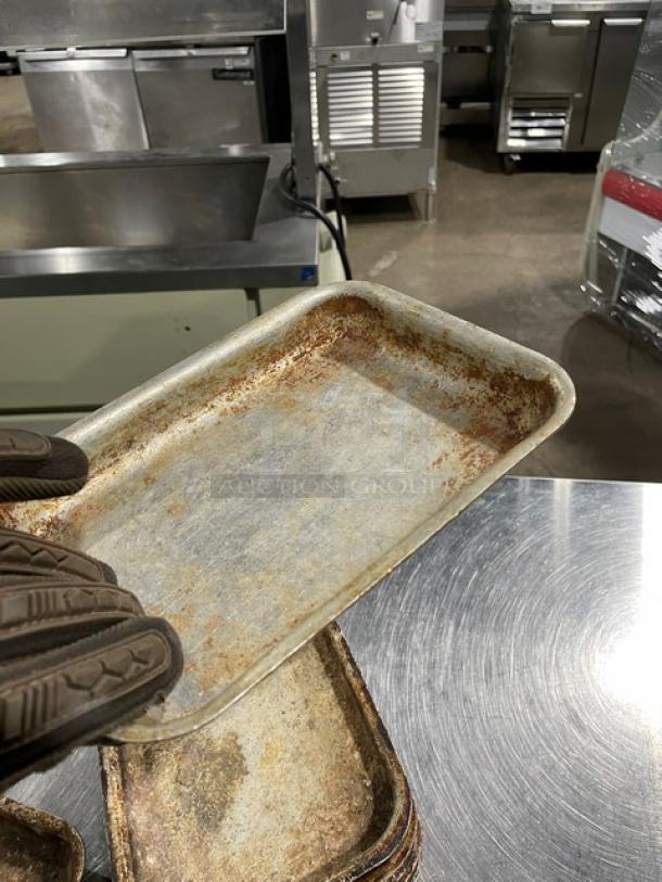 Vintage mini baking pan, worn condition, metallic surface, rectangular shape, held by gloved hand in a commercial kitchen.