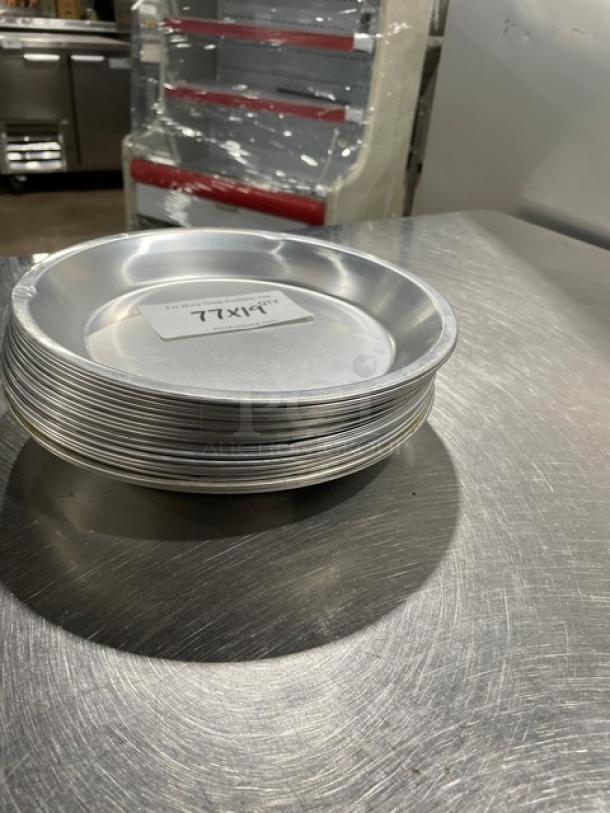 Stack of round commercial pie pans on a metal surface, each with a note "19X" indicating lot size for auction.