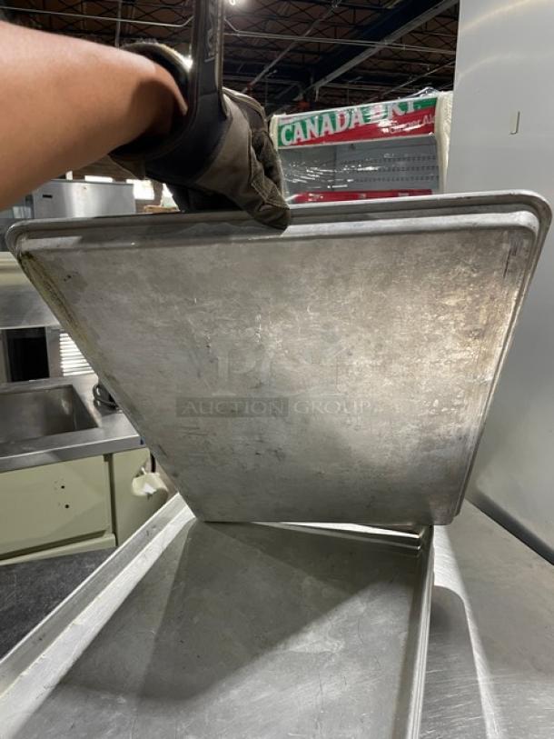 Commercial rectangular baking sheet pan, metal, used condition, held upright showing surface wear and edges.