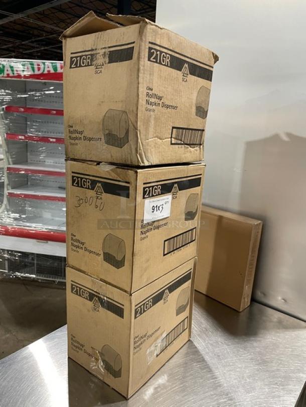 Brand new SCA 21GR Granite RollNap Napkin Dispenser boxes stacked on a table, ready for auction.