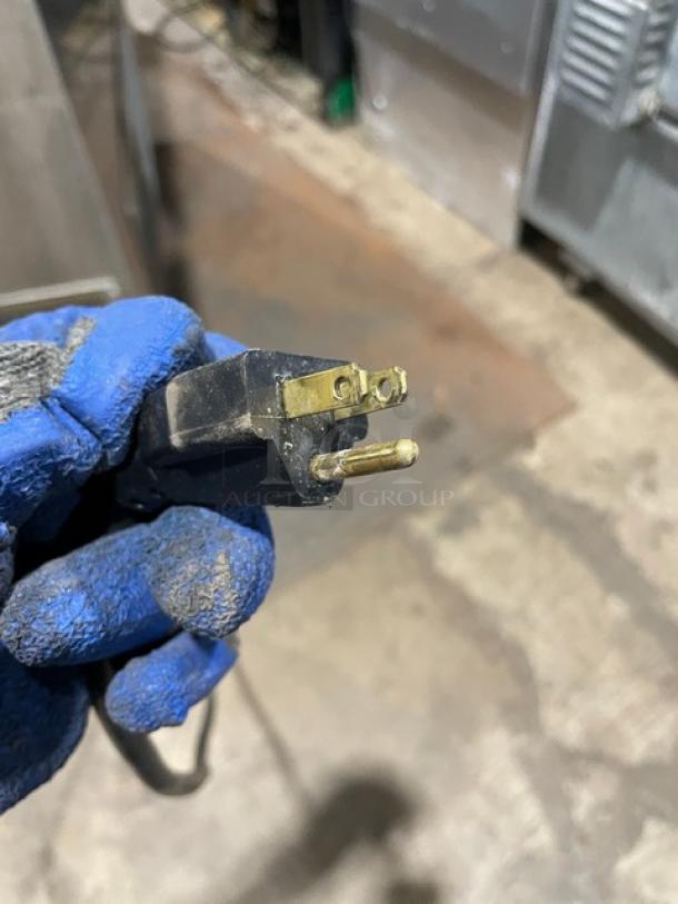 Close-up view of a power plug with gloved hand, indicating part of Universal Coolers undercounter refrigerator setup.