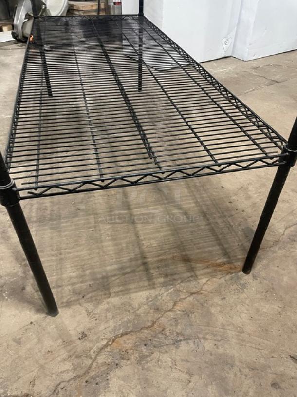 Commercial black 4-tier utility wired rack on legs, metal construction, good condition, suitable for storage or display.