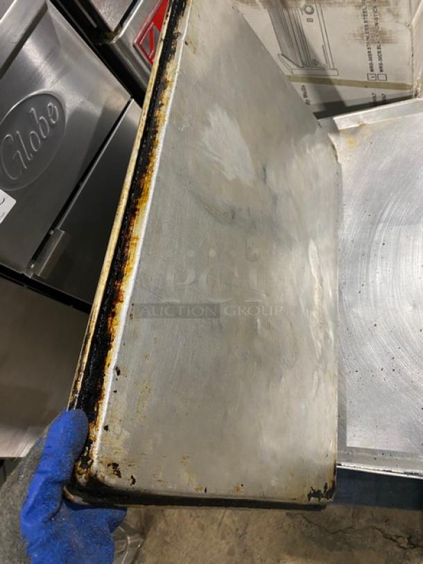 Commercial full-size baking sheet pan with signs of surface wear and discoloration, held with a gloved hand.