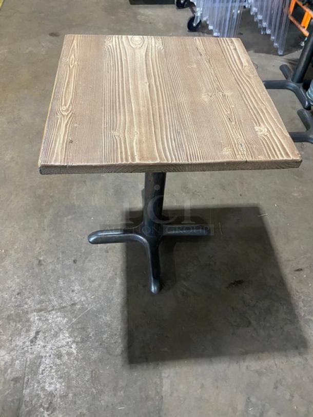 Commercial wooden square dining table with textured wood grain top and sturdy black base, suitable for restaurant use.