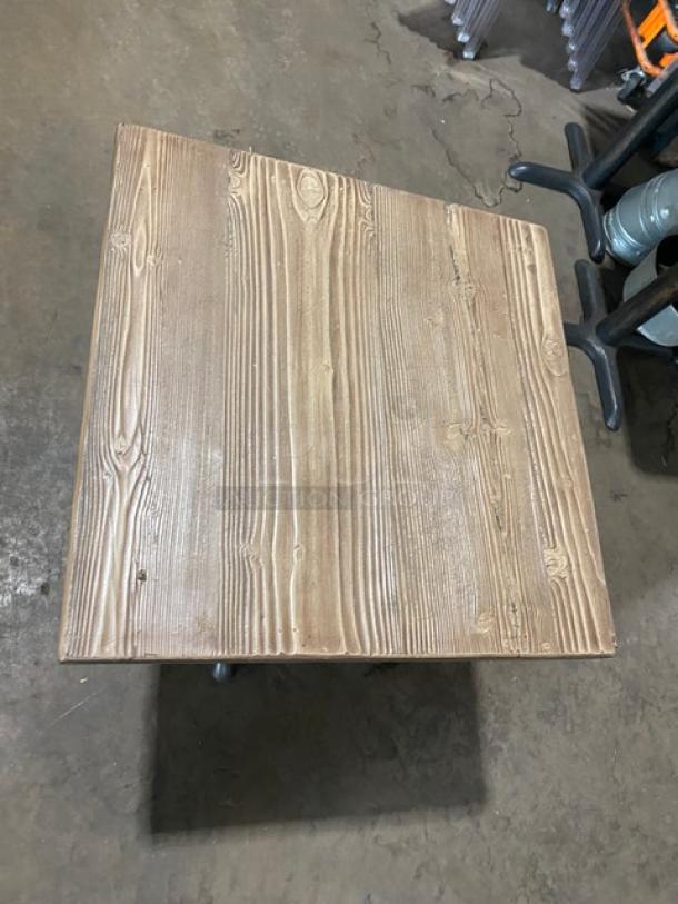 Square wooden dining table with visible grain texture, featuring a sturdy black base. Ideal for commercial use.