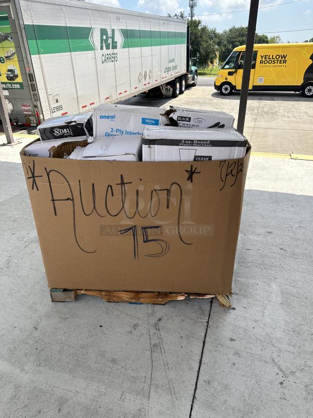 Mixed pallet of packaged items in a large cardboard box labeled "Auction 15" on a wooden pallet.