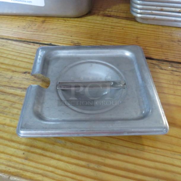 Stainless steel 1/6 size hotel pan lid with handle, used condition, slight wear visible on edges.