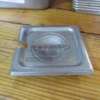 Stainless steel 1/6 size hotel pan lid with handle, used condition, slight wear visible on edges.