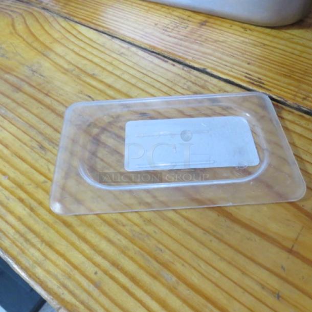 Clear plastic 1/9 size food storage lid on wood surface, rectangular shape, label blank, good condition.