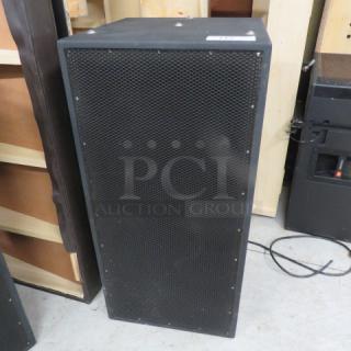 Black subwoofer speaker with metal grille; rectangular shape; used condition; power cable visible.
