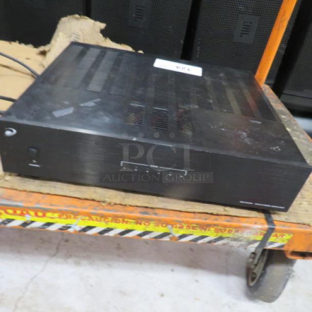 Dayton Audio amplifier, black, showing wear. Ventilation slots on top, front control panel. Power cable attached.
