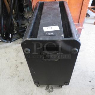 QSC K SUB subwoofer on casters, model K SUB, black, shows wear, includes handle for transport, auction tag 107 visible.