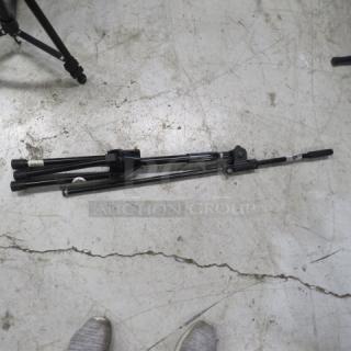 Dr Pro mic stand, folded on concrete floor. Black metal, adjustable height and angle. Good condition, no visible damage.