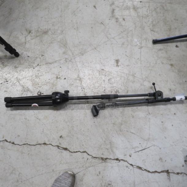 Collapsible black mic stand on concrete floor, adjustable height, good condition.