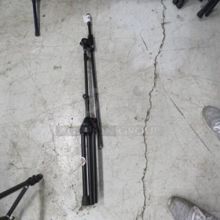 AKG mic stand, black, folded on a concrete floor. Features collapsible legs and adjustable height. Appears lightly used.
