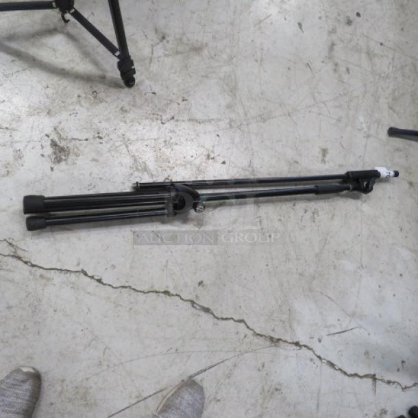 Black mic stand folded on a concrete floor, in good condition, with adjustable legs and mounting hardware.