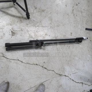 Black mic stand folded on a concrete floor, in good condition, with adjustable legs and mounting hardware.