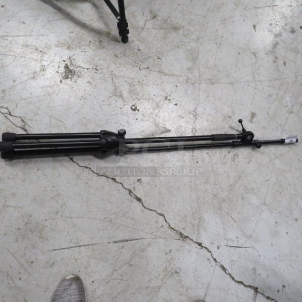 Black telescopic microphone stand with tripod base on a concrete floor. Adjustable height, good condition.