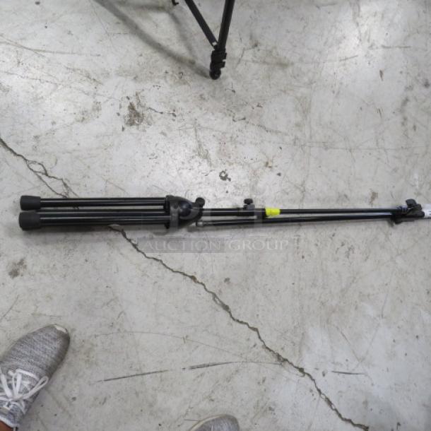 Collapsible mic stand on concrete floor, black metal, adjustable height. Good condition with a yellow tape marking.
