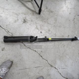 Collapsible mic stand on concrete floor, black metal, adjustable height. Good condition with a yellow tape marking.