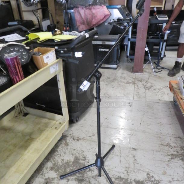 AKG mic stand with adjustable height and boom arm, sturdy tripod base, and visible model label in a warehouse setting.