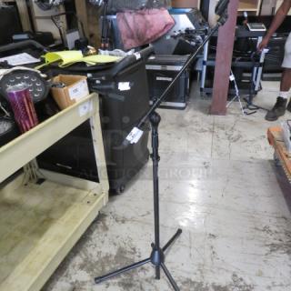 AKG mic stand with adjustable height and boom arm, sturdy tripod base, and visible model label in a warehouse setting.