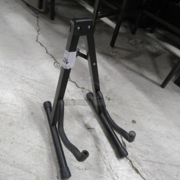 Black metal instrument stand with adjustable arms, label attached. Suitable for supporting guitars or similar instruments.