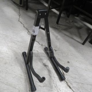 Black metal instrument stand with adjustable arms, label attached. Suitable for supporting guitars or similar instruments.