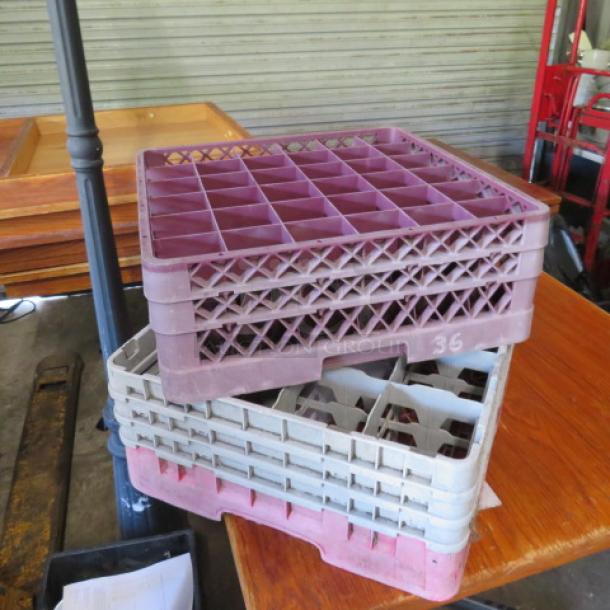 Assorted dishwasher racks, stacked, various colors, used condition, grid design, for industrial kitchen use.