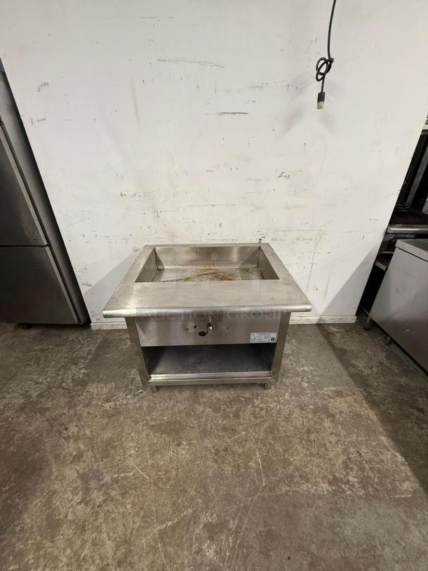 Stainless steel undercounter steam table, durable condition, open storage shelf, label indicates model and serial number.