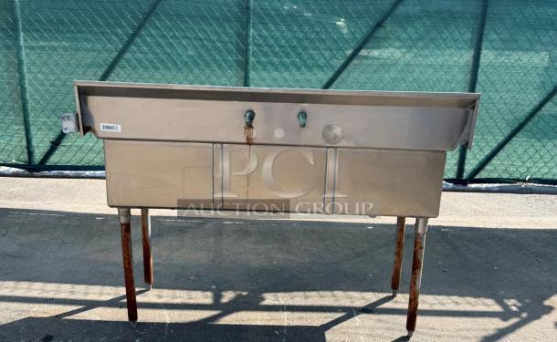 Stainless steel triple sink with rusted legs, dual faucets, and label. Used condition with signs of wear.