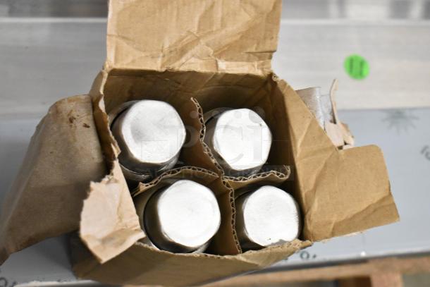 Open cardboard box containing four round metal components, partially wrapped and separated by cardboard dividers.