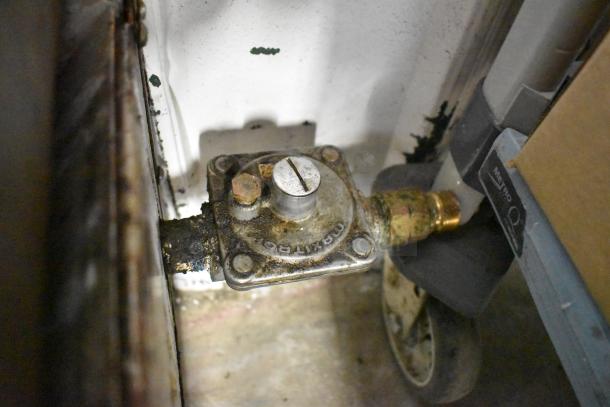 Gas line connection for stainless steel commercial countertop griddle, featuring a worn regulator with "MAXITROL" marking.