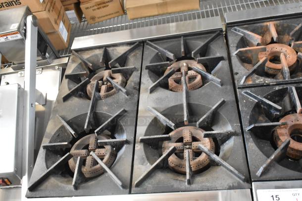 Wells stainless steel 4-burner countertop gas range. Features robust cast-iron grates and controls. Slight wear visible.
