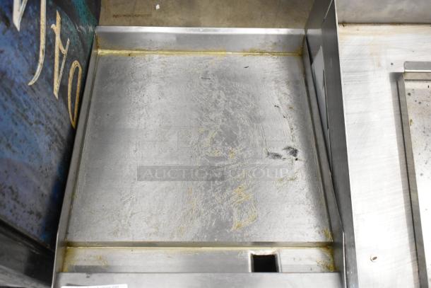 Stainless steel flat top griddle plate, showing wear. Smooth surface with raised edges and a drainage opening.