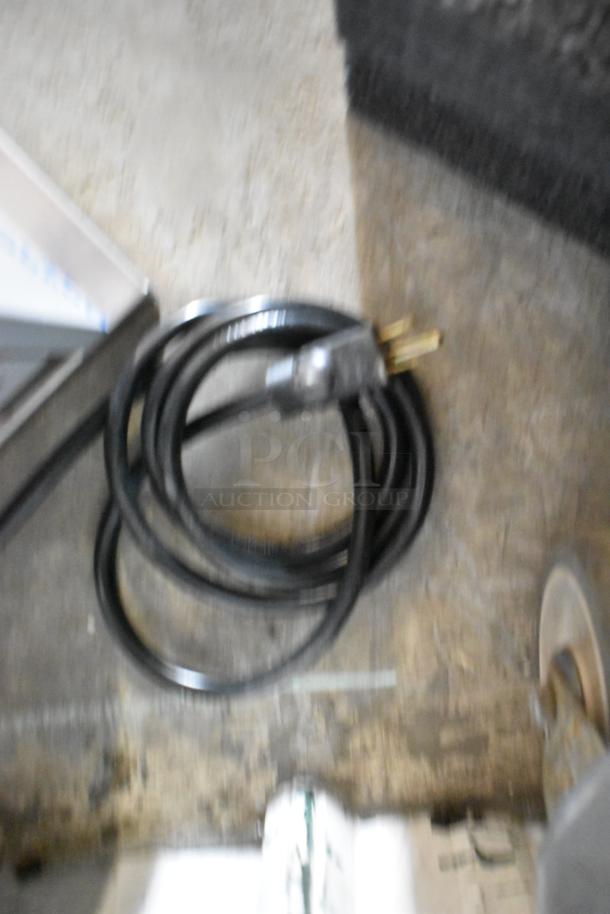 A black power cord for the Prince Castle 296-T55JACK commercial toaster on a concrete floor, showing a three-prong plug.