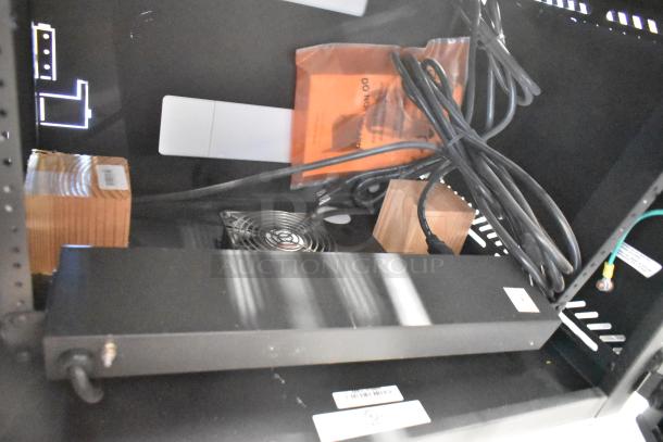 Brand new black metal enclosure system, includes fan, cables, and packaging. Labels indicate model numbers and assembly instructions.