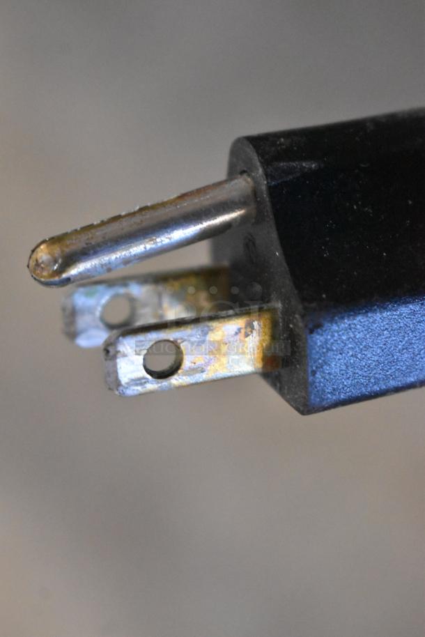 Rusty electrical plug showing wear on metal prongs, with a slightly scratched black casing, indicative of use.