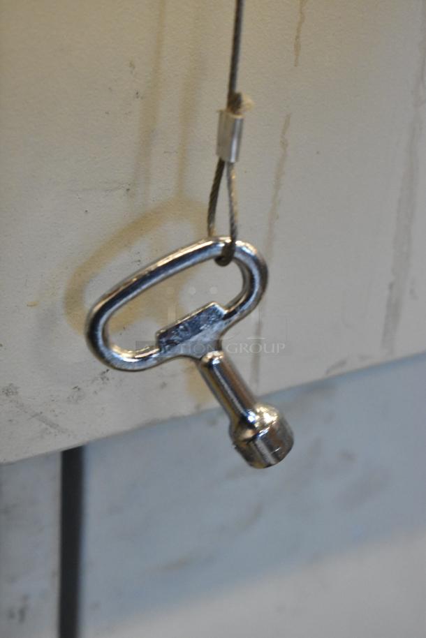 Close-up of metal key dangling, presumably for BlackShields DC0300 cabinet, attached to a thin cable.