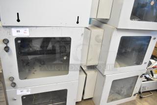 2 new BlackShields DC0300 white metal cabinets, no keys, glass panels, some surface wear, labels indicating auction info.