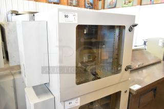 BRAND NEW BlackShields DC0300 white metal cabinet with glass door, visible interior shelving, auction label, and pristine condition.