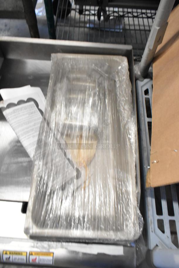 Brand new 2022 Tri Star TSGGM-18i stainless steel natural gas flat top griddle, packaged in plastic wrap, with labels visible.