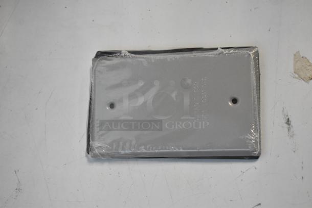 Brand new outlet box cover wrapped in plastic, part of a lot including a pipe mounting kit.