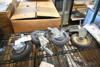 Lot of 4 commercial casters on shelving, each with gray rubber wheels and metal mounts. Tag reads "156 V X4."