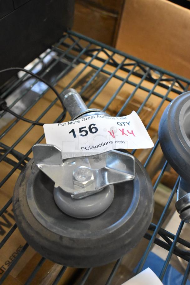 Lot of 4 commercial casters on a wire shelf, each with a sturdy black wheel and metal frame. Tag reads "156 QTY V X4."