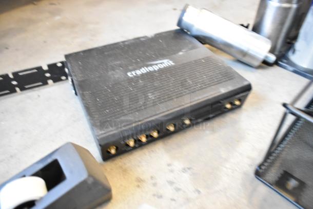 Two poly bins containing various items including a Cradlepoint router, wires, metal legs, tape dispenser, and timer.