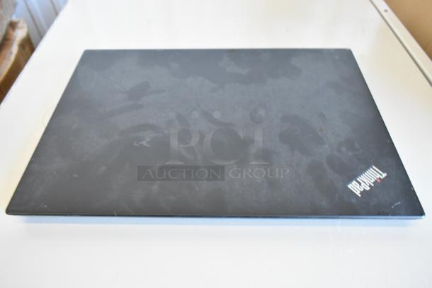 Closed Lenovo ThinkPad laptop lid, showing faint marks, on a white surface.