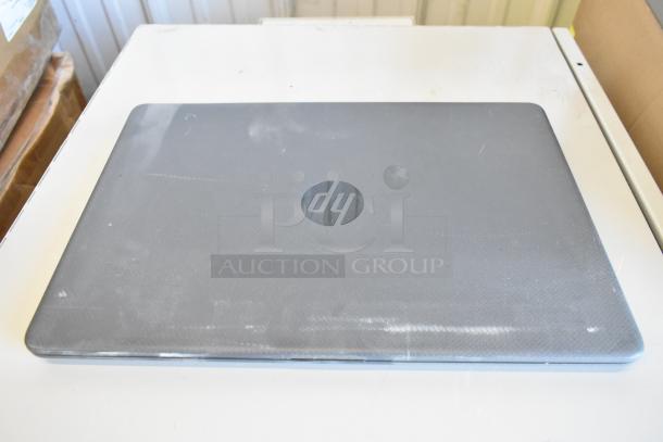 Gray HP laptop, closed, visible wear on lid, HP logo centered. Part of an 11 laptop auction bundle.